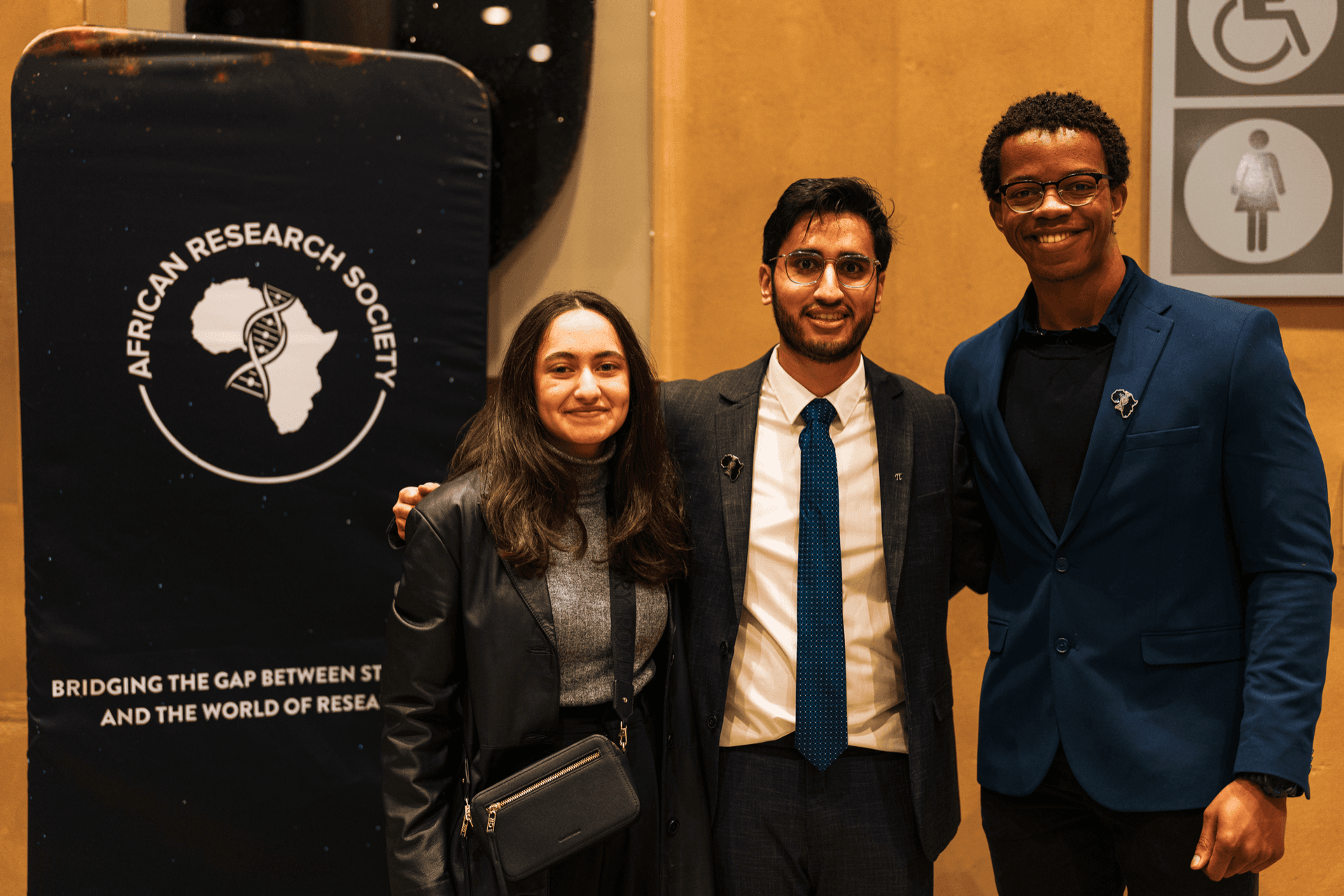Waheed with his friends Zahra and Ramses in front of the African Research Society banner